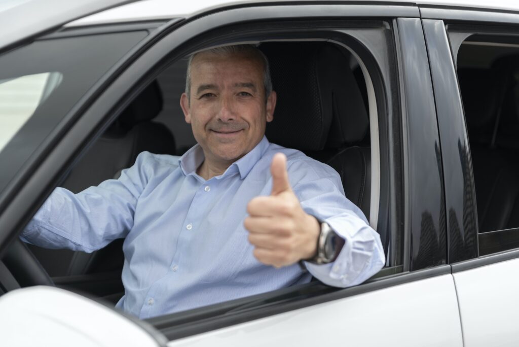 portrait of an elderly driver in car or taxi showing his thumb
